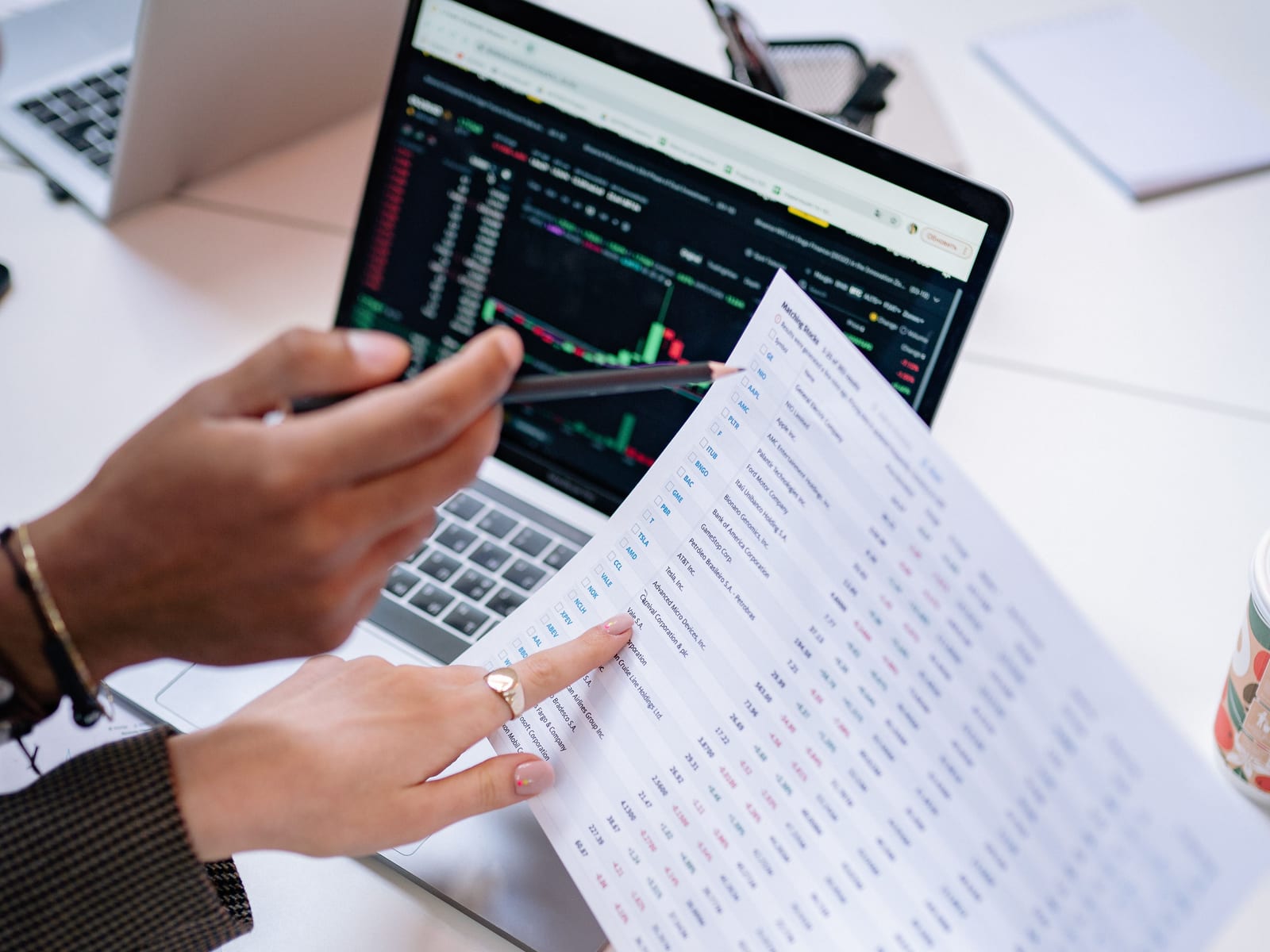 Two colleagues pointing at a printed spreadsheet beside a laptop showing a chart